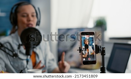 Popular social media influencer recording daily vlog with smartphone while telling stories. Creative digital content creator sitting at home studio desk while broadcasting video podcast. Close up