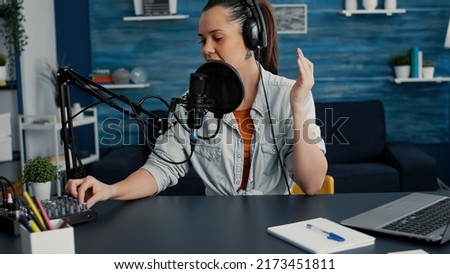 Popular internet streaming influencer putting headphones on and starting to record daily vlog. Social media star sitting at home studio desk while filming podcast video in living room. Studio shoot