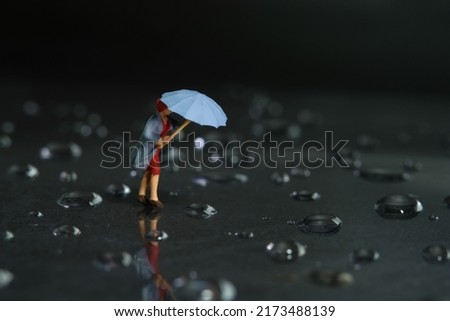 Miniature people toy figure photography. A woman wearing a raincoat using umbrella, walking on the street during a storm, against a very strong wind. Dark cloudy, thunderstorm background. Image photo