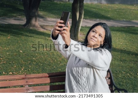 Woman sitting on a park bench taking a selfie