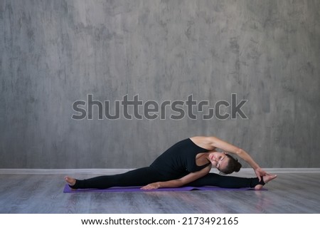 Athletic young woman doing yoga isolated on gray wall background in black sportswear concept of healthy lifestyle and natural balance between body and mental development