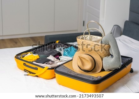 Suitcase for summer vacation on home bed or hotel room with clothes for vacation on tropical beach ocean. Straw hat and bag and swimsuit sunglasses. Concept: travel, tourism, clothing accessories Royalty-Free Stock Photo #2173493507