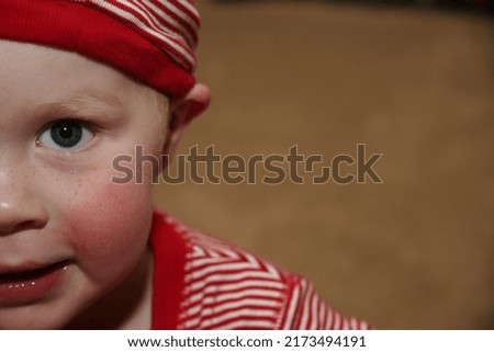 Close up picture of the cutest little Christmas elf looking at the camera with his bright blue toddler eyes.