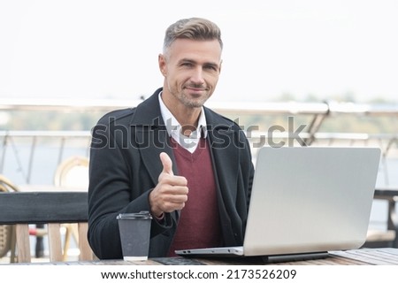 Happy professional guy give thumb making approval gesture working in laptop in outdoor cafe