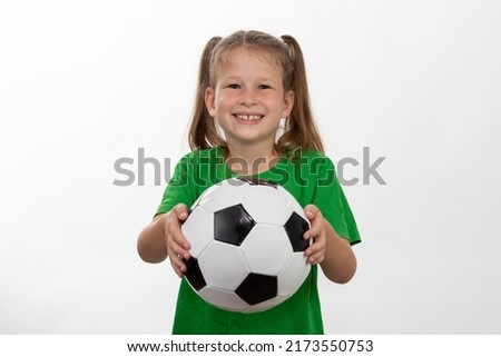 A cute girl in a green t-shirt with a soccer ball in her hand smiles isolated on a white background. A sporty caucasian kid holds the ball. Children's sports game.