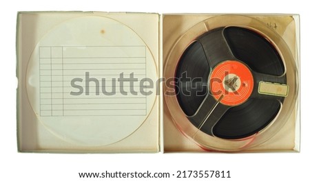 Vintage magnetic audio reel in cardboard box and blank paper tracklist inlay, free copy space. Royalty-Free Stock Photo #2173557811