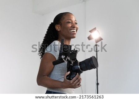 African American Female Videographer Posing with Video Camera in Hand on Film Set. Camera Woman is Proud and Smiling Looking Off Camera. Royalty-Free Stock Photo #2173561263