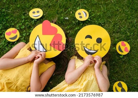 Two people with different cardboard smiles cover their faces lying on the grass. Lover and winking emoticons, top view