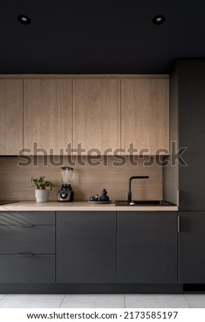 Dark and modern kitchen with black furniture, wooden details and ceiling lamps Royalty-Free Stock Photo #2173585197