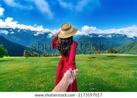 Women tourists holding man's hand and leading him to green pasture and flowers near snow mountain in Georgia. Royalty-Free Stock Photo #2173597017