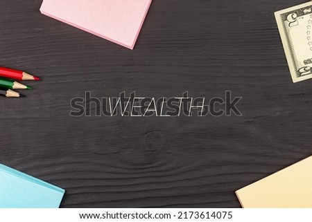 WEALTH - text, money dollars, stickers and colored pencils on a black wooden table. Business concept: buying, selling, commerce (copy space).