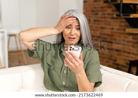 Worried senior woman staring at a smartphone screen at home, upset retire female sitting on the couch looks at mobile phone with vexation, read terrible news or received bad analysis results Royalty-Free Stock Photo #2173622469