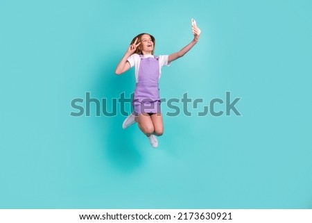 Full size photo of overjoyed carefree girl jump hold phone make selfie demonstrate v-sign isolated on teal color background