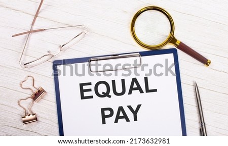 A tablet with the text EQUAL PAY on white paper, a magnifier, glasses, golden paper clips and a pen lie on a white office table. Top view, flat lay.