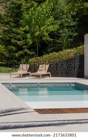 Vertical view of swimming pool area in the garden of the house with wooden sun loungers and pool shutter