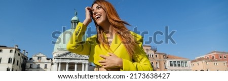 low angle view of redhead woman laughing near medieval buildings in Venice, banner