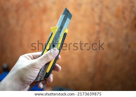The serviceman is holding a big cutter knife, the utility hand tool using at factory workplace. Industrial working and object photo. Royalty-Free Stock Photo #2173639875