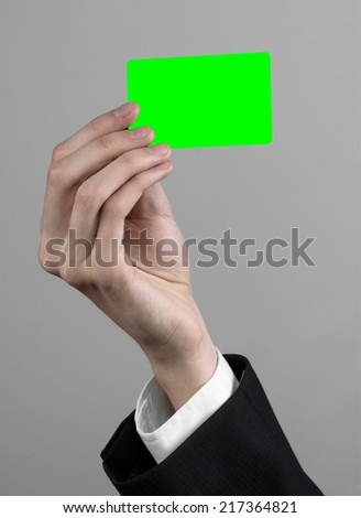 businessman in a black suit and black tie holding a card, a hand holding a card, green card,  card is inserted, the green chroma key card, gray background, isolated, business theme,  theme of banking