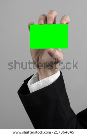 businessman in a black suit and black tie holding a card, a hand holding a card, green card,  card is inserted, the green chroma key card, gray background, isolated, business theme,  theme of banking