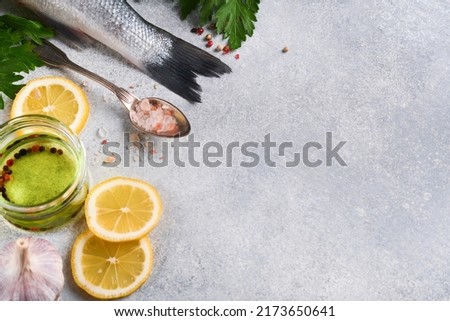 Fresh fish. Sea Bass raw with salt, pepper, parsley, olive oil and lemon on cutting board on light gray concrete rustic background. Food cooking background. Top view, copy space.