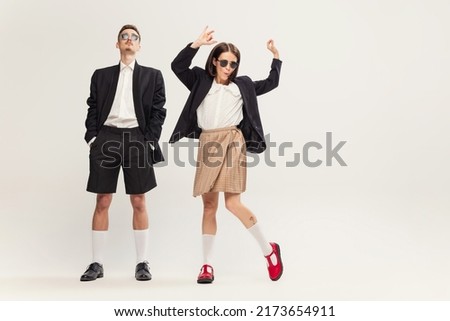 Portrait of stylish young couple, man and woman in retro suit posing isolated over grey studio background. Cheerful dance. Emotions. Concept of retro fashion, art photography, style, queer, beauty