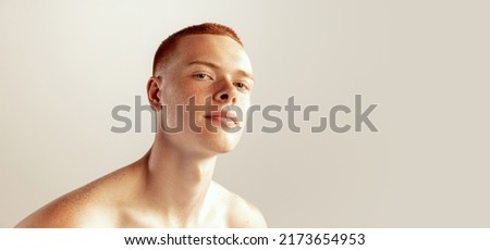 Portrait of handsome young red-haired man with freckles posing, barely smiling, looking at camera isolated over grey studio background. Concept of men's health, lifestyle, beauty, body and skin care Royalty-Free Stock Photo #2173654953