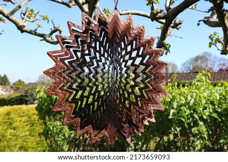 A brown metal ornament in the shape of a spiral star hanging from the branch of a tree Royalty-Free Stock Photo #2173659093