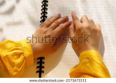 Horizontal photo. Woman is learning reading guide for low vision. Women's hands with yellow sleeves on a tutorial in Braille font. January 4. World sight day. International day of visual impairment.