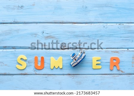 Colorful letters and decorative boat laid out in the word "Summer"on blue wooden background.