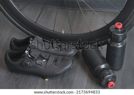 stylish road bike shoes, cycling water bottles and a carbon black wheel closeup concept Royalty-Free Stock Photo #2173694833