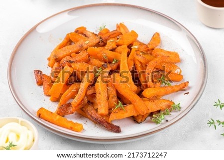Tasty homemade roasted sweet potato with herbs, salt and pepper roasted in the pan on a ceramic plate and mayo, on a light grey table background, close up