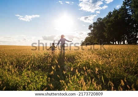 unrecognizable child and woman, mother and son, run across a yellow meadow towards the sun. Happy childhood, have fun on the walk. Forward to a bright future. back view. Backlight and soft focus Royalty-Free Stock Photo #2173720809