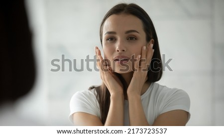 Taking care of face. Mirror reflection of pretty young female visually checking skin health, doing morning skincare procedures, making rejuvenating facial massage before applying decorative cosmetics Royalty-Free Stock Photo #2173723537