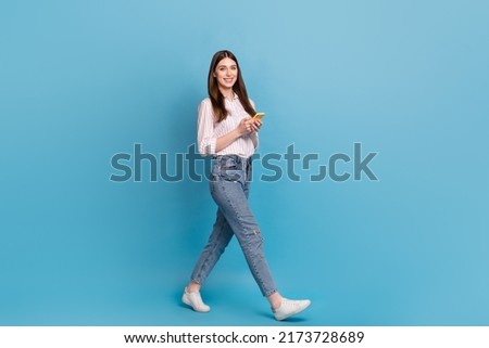Full length body size view of attractive cheerful trendy girl using gadget strolling isolated over bright blue color background