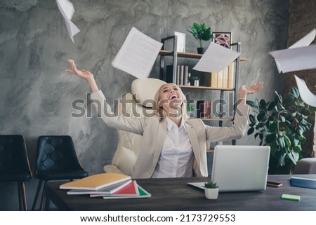 Photo of excited delighted business person sit chair hands throw papers air fly workplace loft modern office
