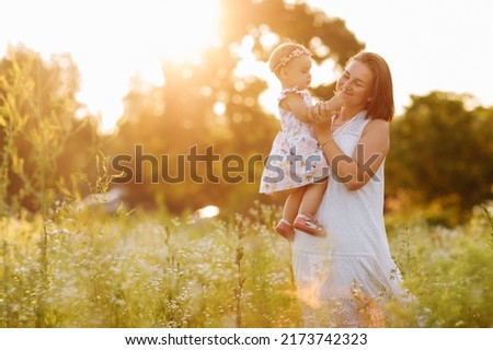 Happy young mother playing with her little baby daughter on sunshine warm spring or summer day. Beautiful sunset light in the garden or in the park. Happy family concept