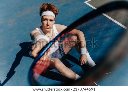 Portrait of a healthy athletic man in retro style with an athletic build with a tennis racket. Redhead guy playing tennis on the sports ground. Portrait of a healthy athletic man with an  Royalty-Free Stock Photo #2173744591