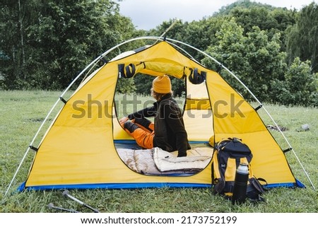 Summer camping in a tent, a person sitting in a campsite and enjoying nature, a yellow tourist tent, a tourist on a camping holiday. High quality photo
