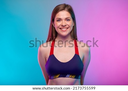 Smiling sporty woman in fitness bra sportswear with hands behind back. Female fitness portrait isolated on neon colored background.