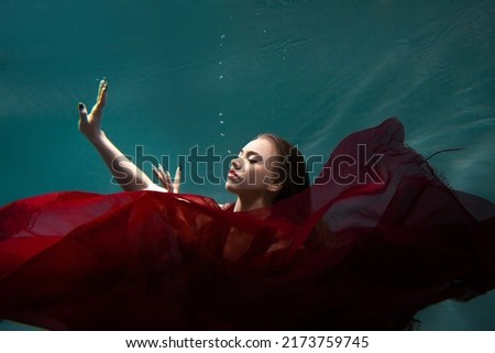 Underwater shooting, a beautiful young woman in a red dress is swimming under the surface of the water. Fabulous photo refraction under water.