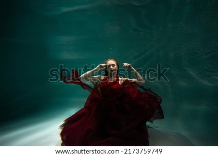 Underwater shooting, a beautiful young woman in a red dress is swimming under the surface of the water. Fabulous photo refraction under water.