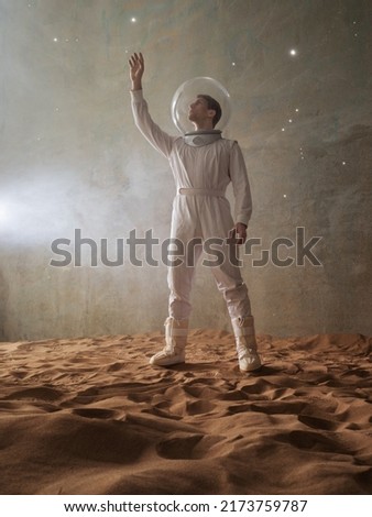 a man in a white futuristic spacesuit explores the planet, an astronaut in an empty colony on the sand, a holographic star map on the background Royalty-Free Stock Photo #2173759787