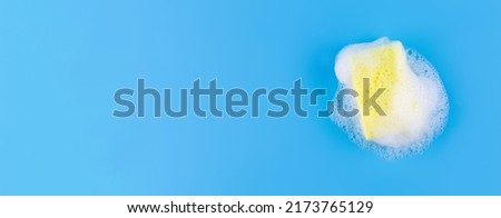 Cleaning yellow sponge and a soapy bubble foam on a blue background. Cleaning concept, cleaning service. Banner. Flat lay, top view