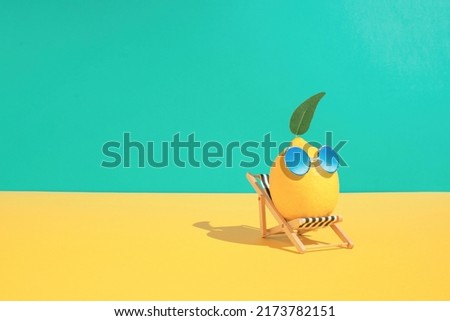 Lemon fruit chilling in beach chair on the blue and yellow background. Summer vacation concept. Sunglasses on lemon with green leaf relaxing on the sunbed. Creative art minimal aesthetic.