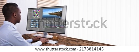 An African American Businessman Editing The Video On Computer Over The Wooden Desk