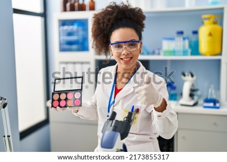 Young african american woman working at scientist laboratory doing make up smiling happy and positive, thumb up doing excellent and approval sign 