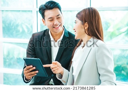 Business couple standing together with baggage and checking flight time on tablet near the window at the departure area at the airport