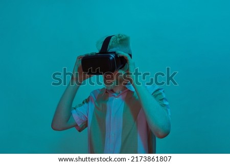 Albino caucasian guy putting on head Virtual reality glasses. Young bearded blonde man wearing t-shirt. Modern entertainment and leisure. Isolated on blue background. Studio shoot. Copy space