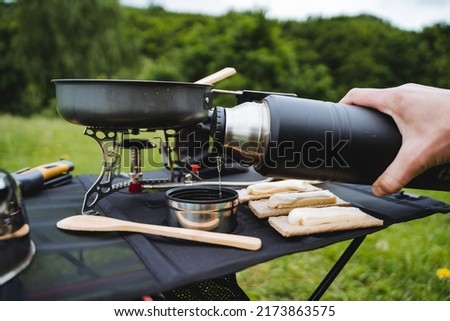 A person holds in his hand a thermos with tea, pour water into a mug in nature, food on a hike, a camping table, breakfast in nature, tourist dishes, compact equipment. High quality photo