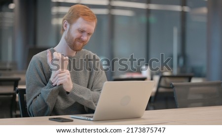 Young Man having Wrist Pain while using Laptop in Office 